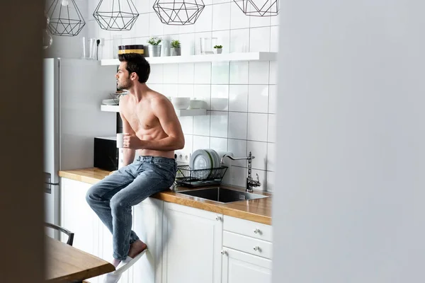 Сексуальный мужчина без рубашки держа чашку кофе на кухне утром — стоковое фото