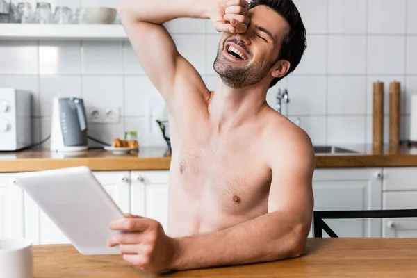 Веселый сексуальный мужчина без рубашки с помощью цифрового планшета на кухне — стоковое фото
