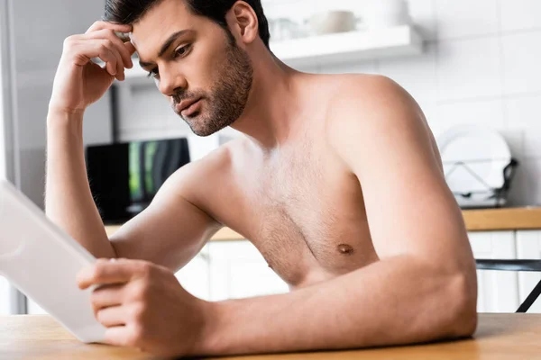 Сексуальный задумчивый мужчина без рубашки с помощью цифрового планшета на кухне — стоковое фото