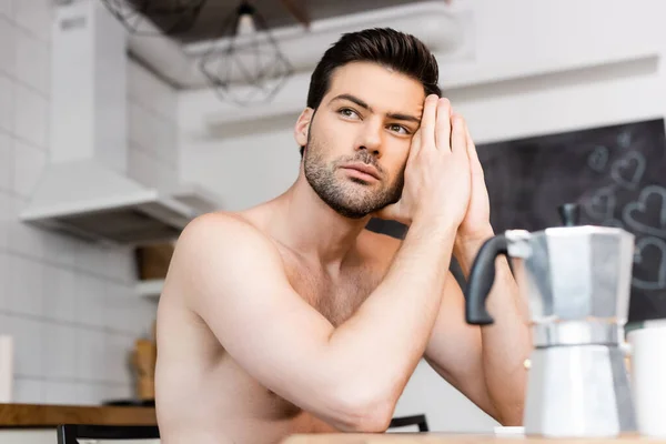 Nachdenklicher hemdsloser trauriger Mann sitzt mit Kaffeekanne in der Küche — Stockfoto