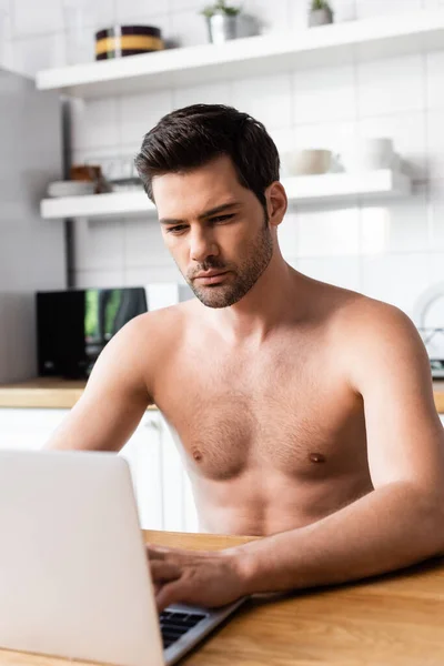 Sexy shirtless male freelancer working on laptop on kitchen — Stock Photo