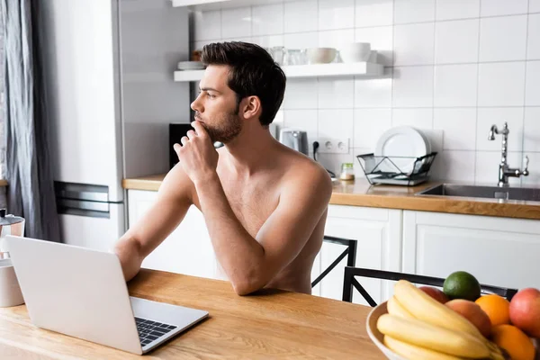 Pensive shirtless freelancer working on laptop on kitchen — Stock Photo