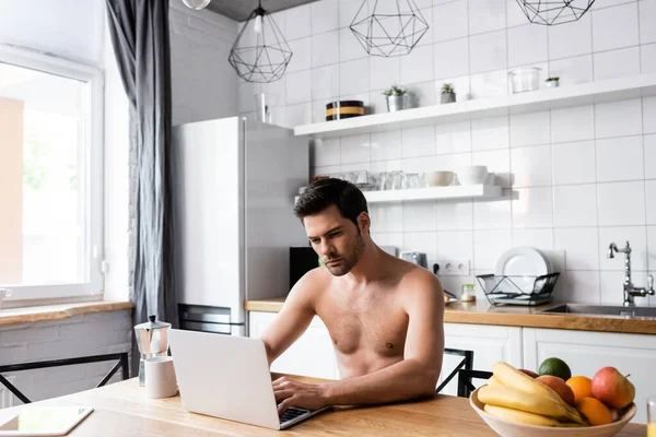 Handsome shirtless freelancer working on laptop on kitchen with fruits and coffee — Stock Photo