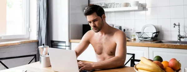Сексуальний фрілансер без сорочки, що працює на ноутбуці на кухні з фруктами та кавою, заголовок веб-сайту — стокове фото