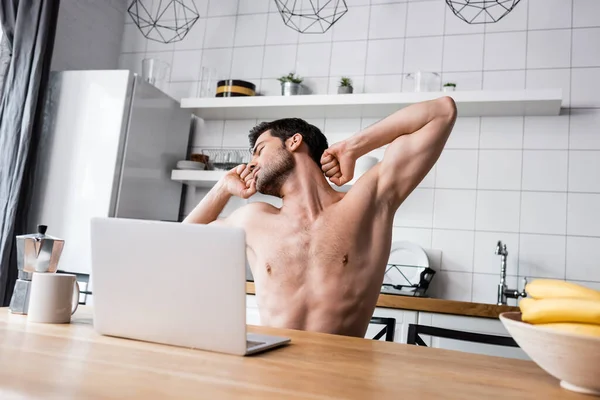 Sexy shirtless freelancer stretching while working on laptop on kitchen with coffee — Stock Photo