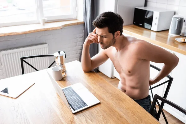 Thoughtful shirtless freelancer working on laptop on kitchen with coffee — Stock Photo