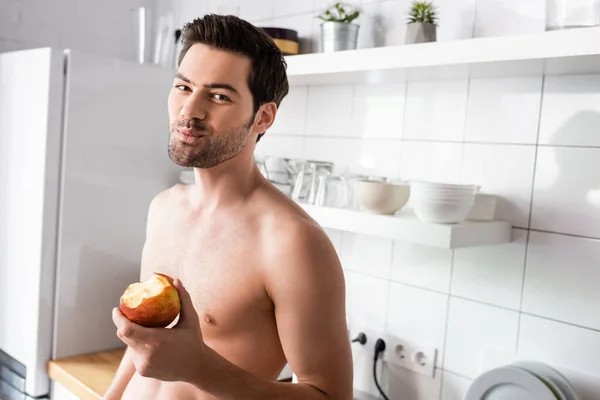 Мужчина без рубашки ест яблоко на кухне утром — стоковое фото