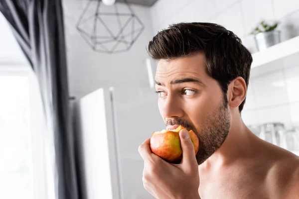 Sorprendido hombre sin camisa comiendo manzana en la cocina - foto de stock