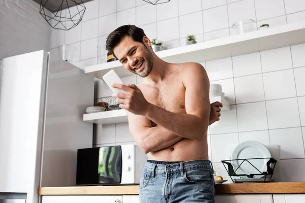 Sexy laughing man using smartphone in kitchen at home — Stock Photo