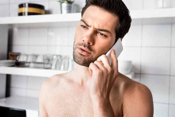 Homem sem camisa preocupado falando no smartphone na cozinha em casa — Fotografia de Stock