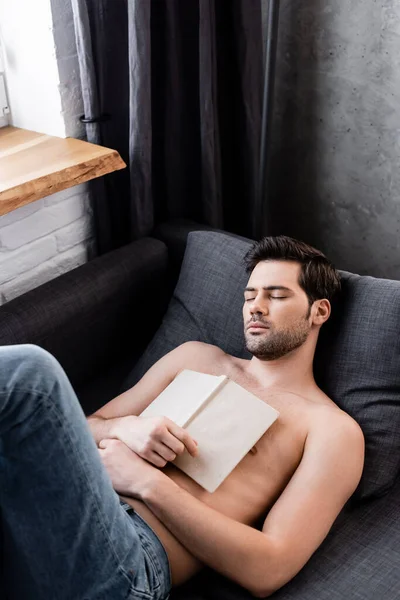 Сексуальний без сорочки чоловік спить з книгою на дивані — стокове фото