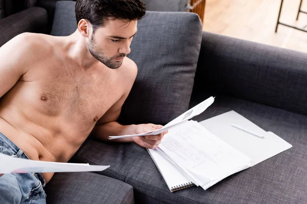 Sin camisa freelancer masculino haciendo papeleo en el sofá durante la cuarentena - foto de stock