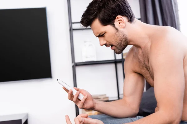 Hombre sin camisa enojado mirando el mando a distancia desde el aire acondicionado en casa - foto de stock