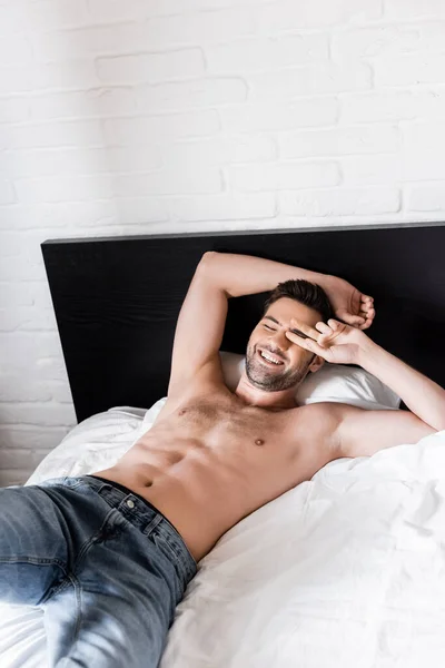 Schöner hemdsloser lächelnder Mann, der es sich zu Hause auf dem Bett gemütlich macht — Stockfoto