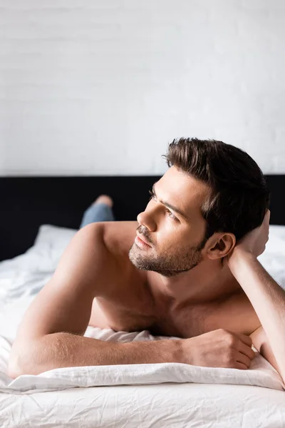 Handsome dreamy shirtless man relaxing on bed at home — Stock Photo