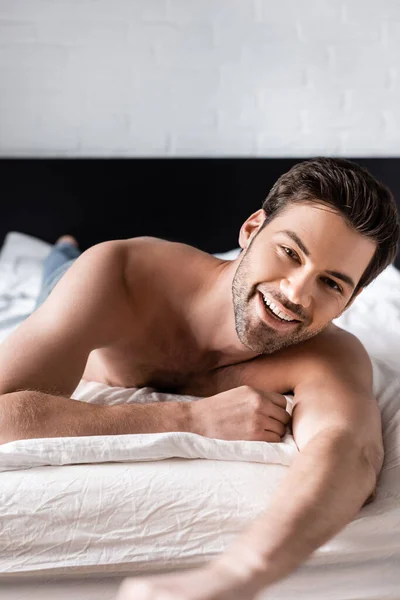 Cheerful handsome shirtless man lying on bed at home — Stock Photo