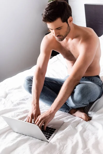 Freelancer muscular bonito trabalhando no laptop na cama — Fotografia de Stock