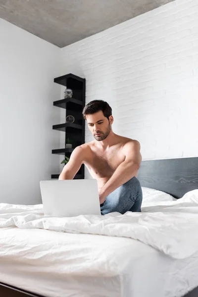 Guapo sin camisa freelancer trabajando en el ordenador portátil en la cama en casa - foto de stock