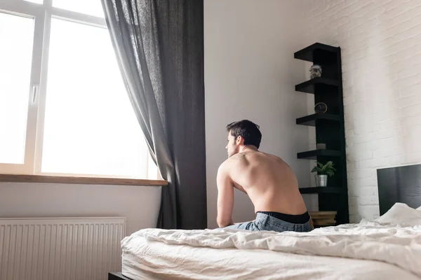 Сексуальный грустный мужчина без рубашки сидит на кровати — стоковое фото