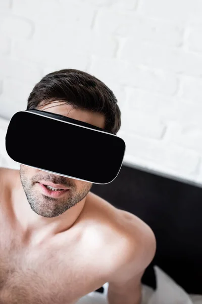 Hombre sin camisa guapo usando auriculares de realidad virtual en la cama - foto de stock