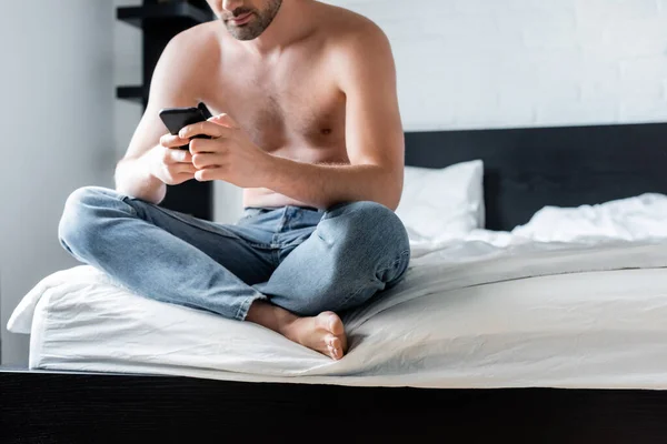 Vista cortada do homem sem camisa usando smartphone na cama em casa — Fotografia de Stock