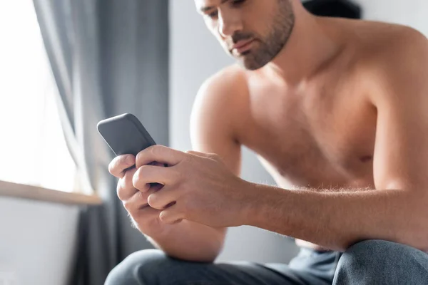 Schöner Mann ohne Hemd mit Smartphone auf dem Bett zu Hause — Stock Photo