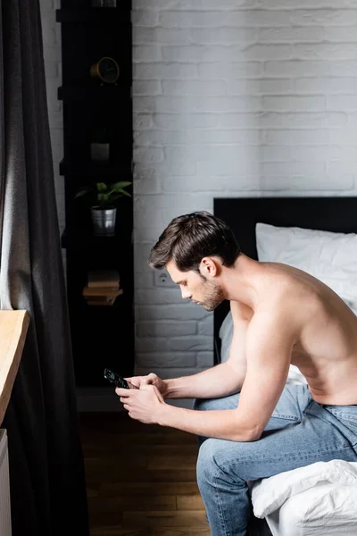 Красивый мужчина без рубашки с помощью смартфона дома — стоковое фото