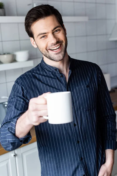 Alegre guapo hombre sosteniendo taza de café en casa en cuarentena - foto de stock