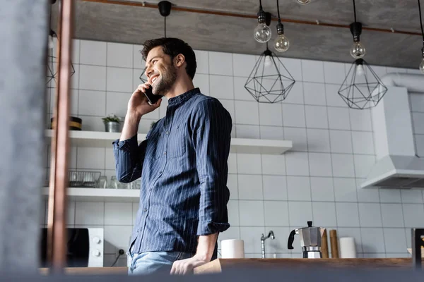 Smiling man talking on cellphone on kitchen with coffee pot and cup during quarantine — Stock Photo