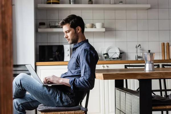 Handsome freelancer working laptop with blank screen on kitchen with coffee pot during self isolation — Stock Photo