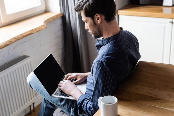 Hombre guapo de red portátil con pantalla en blanco en la cocina con taza de café durante la cuarentena — Stock Photo