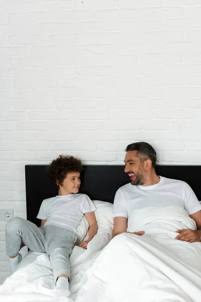 Curly boy and bearded father looking at each other in bedroom — Stock Photo