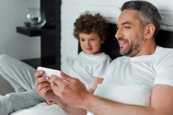 Selektiver Fokus des bärtigen Vaters, der Smartphone in der Nähe seines Sohnes hält — Stockfoto