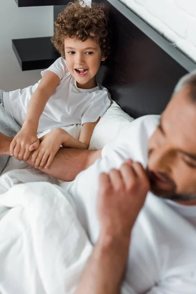 Селективное внимание кудрявого ребенка, смотрящего на счастливого отца в спальне — стоковое фото