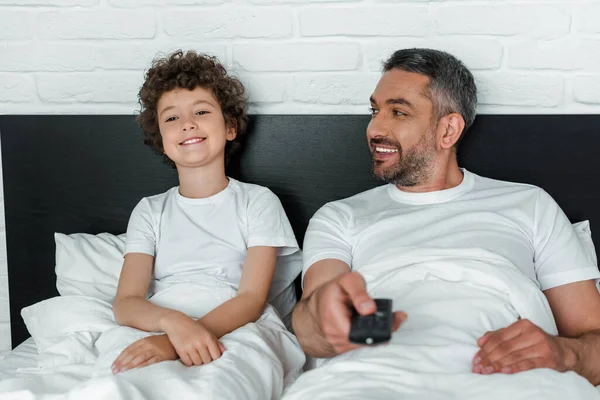 Messa a fuoco selettiva di padre felice guardando figlio allegro e tenendo telecomando — Foto stock