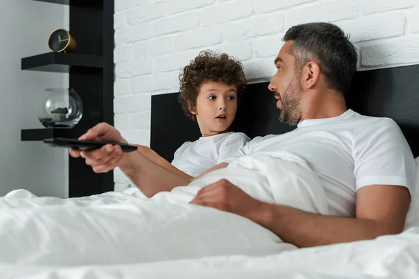 Selective focus of surprised father holding remote controller near curly son — Stock Photo