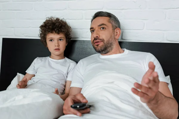 Selektiver Fokus des Vaters gestikuliert, während er Fernbedienung in der Nähe des lockigen Sohnes hält — Stockfoto