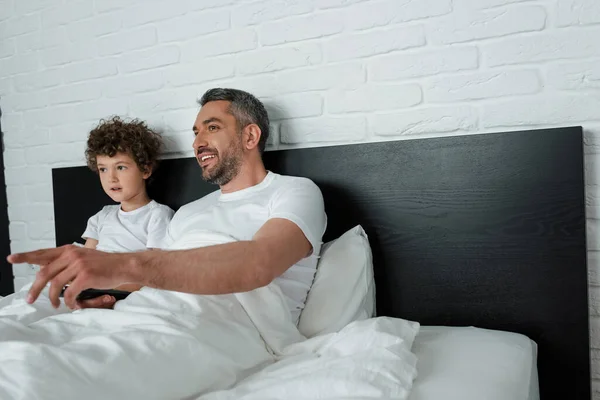 Enfoque selectivo de padre feliz señalando con el dedo mientras ve la película con su hijo - foto de stock