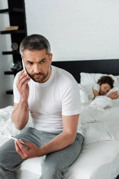 Selektiver Fokus des Menschen mit digitalem Thermometer, der in der Nähe eines kranken Kindes mit dem Smartphone spricht — Stockfoto