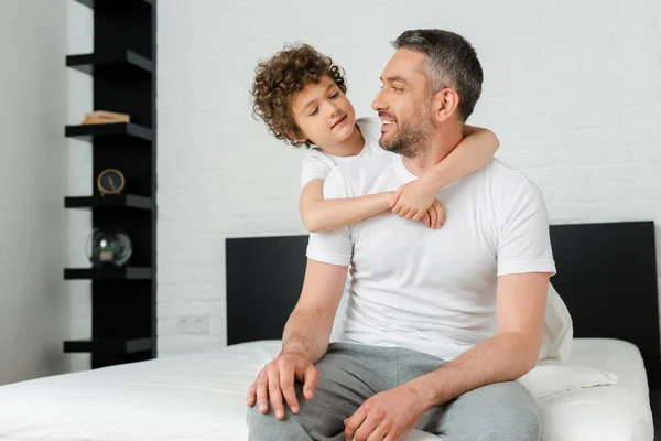 Rizado hijo abrazando alegre barbudo padre en el dormitorio - foto de stock