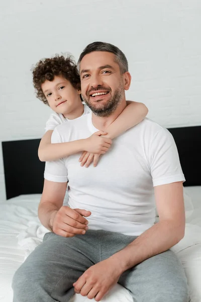 Encaracolado filho abraçando feliz pai barbudo no quarto — Fotografia de Stock