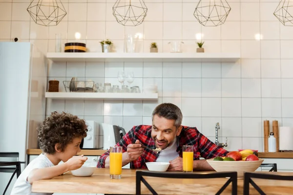 Glücklicher Vater und lockiger Sohn essen leckere Cornflakes in der Küche — Stockfoto