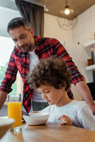 Foyer sélectif de fils bouclés regardant bol près du père dans la cuisine — Photo de stock