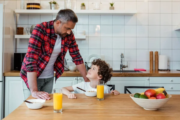 Веселий хлопчик дивиться на гарного батька біля сніданку на столі — стокове фото