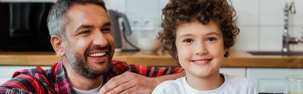 Ein fröhlicher Vater blickt seinen lächelnden und lockigen Sohn an — Stockfoto