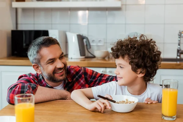 Selektive Fokussierung des fröhlichen Vaters auf den glücklichen und lockigen Jungen beim Frühstück auf dem Tisch — Stockfoto