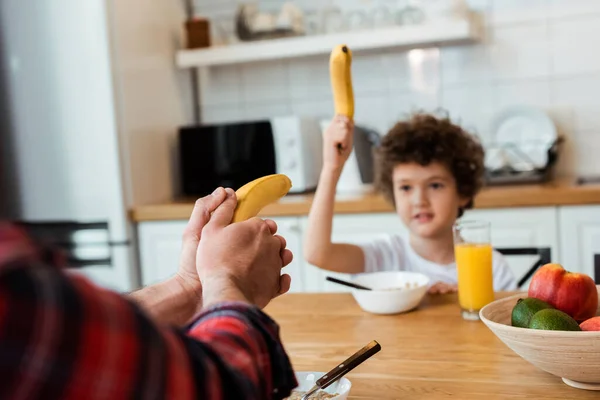Selective focus of father and son holding bananas while playing in kitchen — Stock Photo