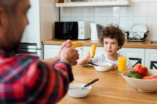 Selective focus of father and curly son holding bananas while playing in kitchen — Stock Photo