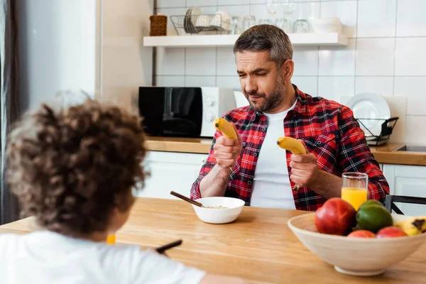 Selektiver Fokus des Vaters, der frische Bananen in der Nähe von Lockenkopf und Frühstück auf dem Tisch hält — Stockfoto