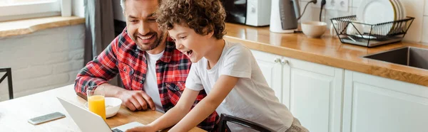 Orientação panorâmica de criança alegre usando laptop perto do pai freelancer — Fotografia de Stock